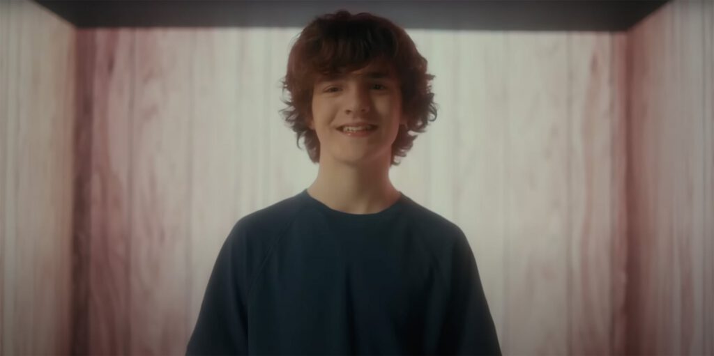 Teen boy smiling indoors in front of softly lit curtains.