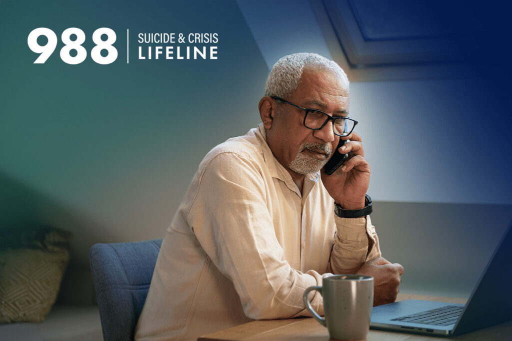 Man sitting at a laptop talking on the phone with “988 Suicide & Crisis Lifeline” text on the image.