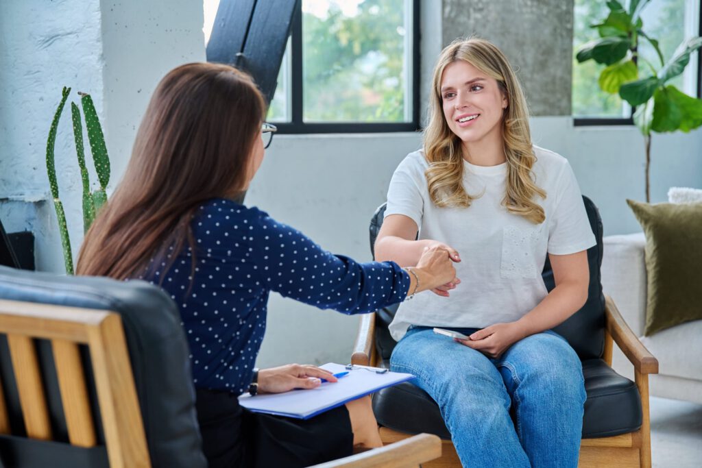 Smiling young woman shaking hands with therapist at first counseling appointment
